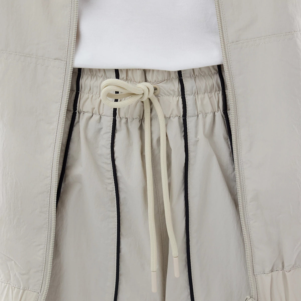 New Era New York Yankees MLB Piping Track Cream Track Pants, close-up view showing the elasticated waistband with cream drawstring, contrasting black piping along the seams, and a glimpse of matching jacket edges.