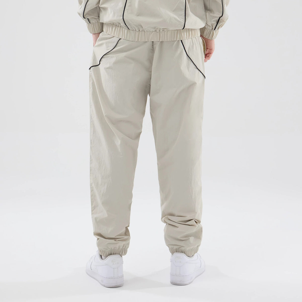 New Era New York Yankees MLB Piping Track Cream Track Pants, back view on a model with hands in pockets, showing black piping detail along the side seams, elasticated waistband and cuffs, and a relaxed fit over white trainers.