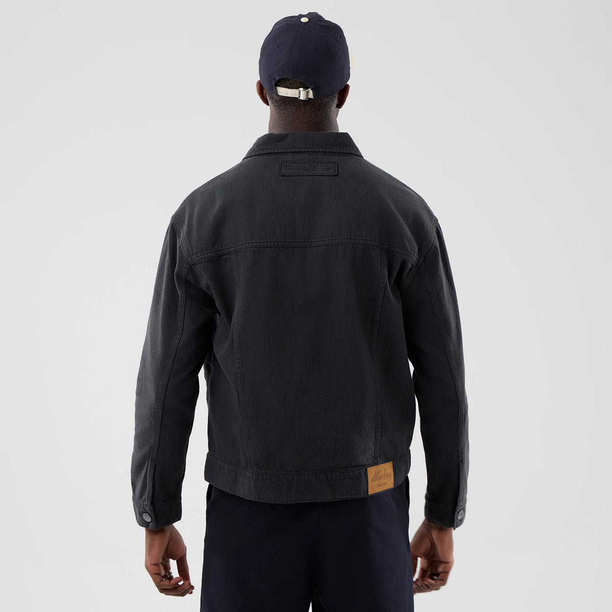 New Era New York Yankees MLB Stripe Denim Grey Jacket, back view showing a model wearing the jacket, with a small New Era patch on the upper back and a leather patch near the lower hem, matched with a dark cap and trousers.