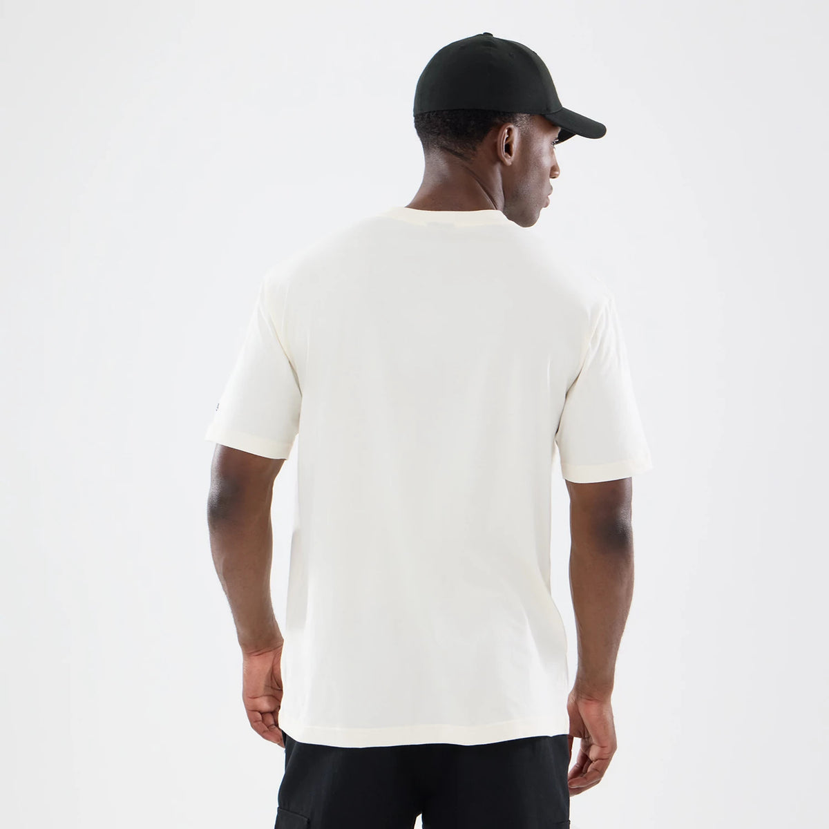 New Era Denver Broncos NFL Sport Classic Cream T-Shirt, back view on a model, showing the plain cream back of the T-shirt with short sleeves and a relaxed fit, styled with a black cap and dark trousers.