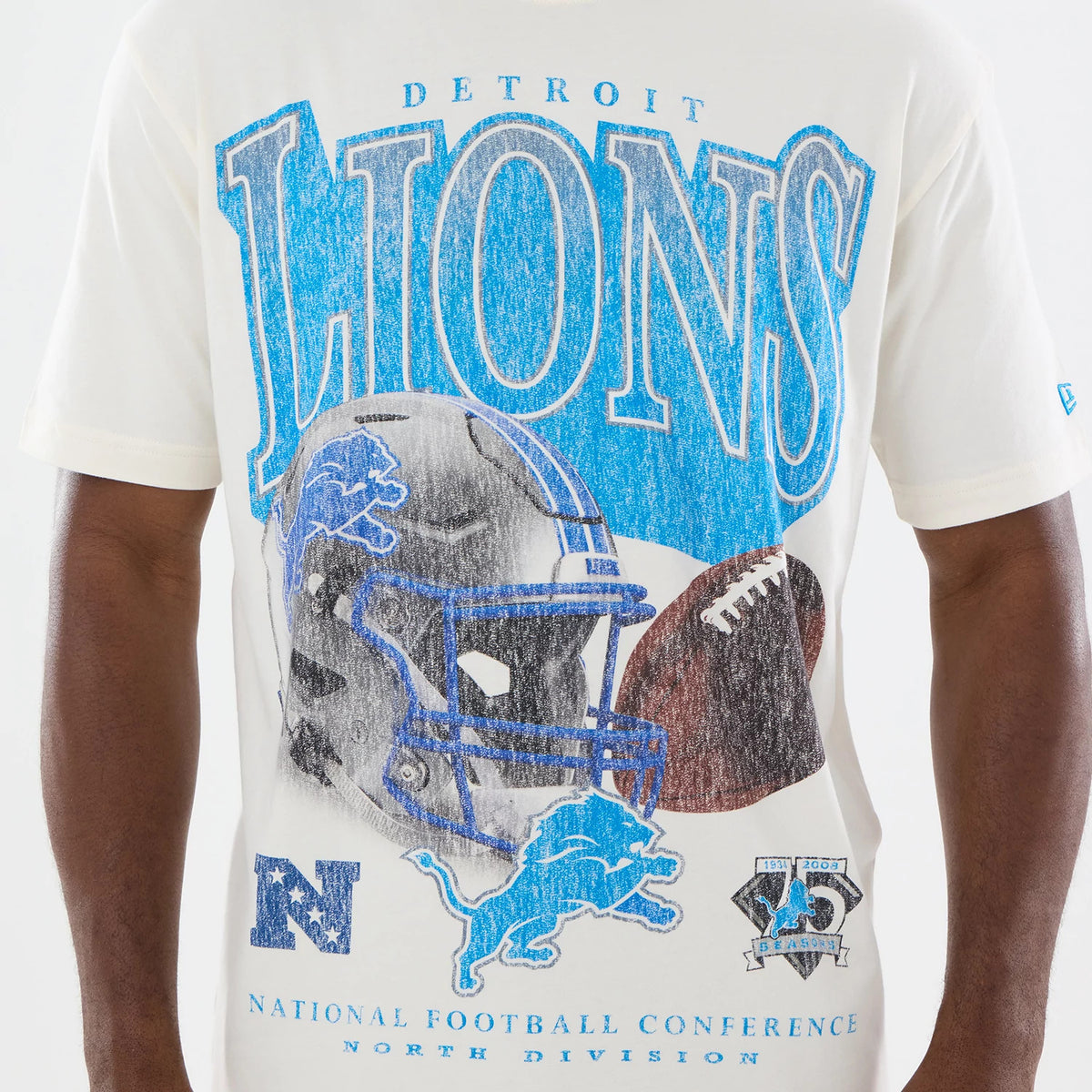 New Era Detroit Lions NFL Sport Classic Cream T-Shirt, front view featuring a large blue and grey Lions graphic with a football helmet, a football, and the Detroit lettering. An embroidered New Era logo is on the left sleeve.