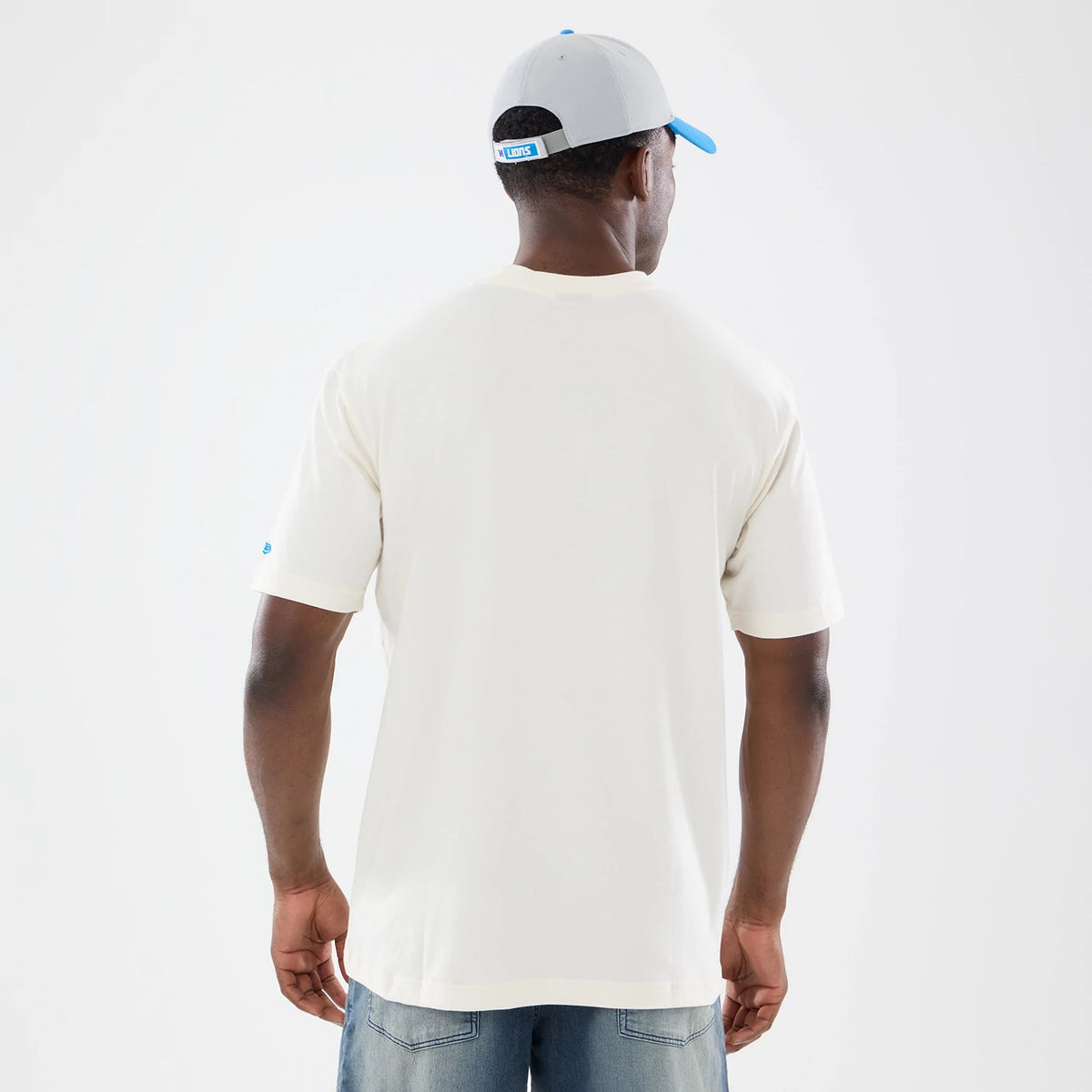 New Era Detroit Lions NFL Sport Classic Cream T-Shirt, back view on a model wearing a grey cap, showing a plain cream back with the sleeve featuring an embroidered New Era logo in blue near the bottom hem.