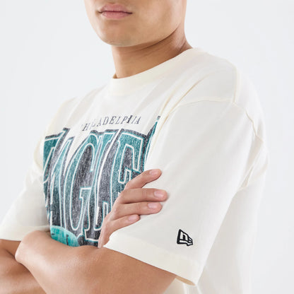 New Era Philadelphia Eagles NFL Sport Classic Cream T-Shirt, front view on-model showing a distressed logo across the chest in teal and black, with the New Era embroidered logo in black near the cuff of the short sleeve.