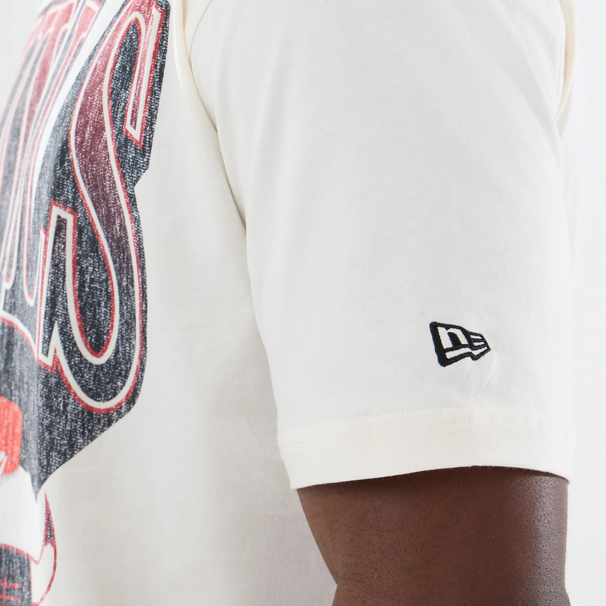 New Era Chicago Bulls NBA Sport Classic Cream T-Shirt, side view showing the arm with a small black embroidered New Era logo on the sleeve, a large vintage Bulls graphic in red and black across the chest, and cream fabric extending to the shoulder.