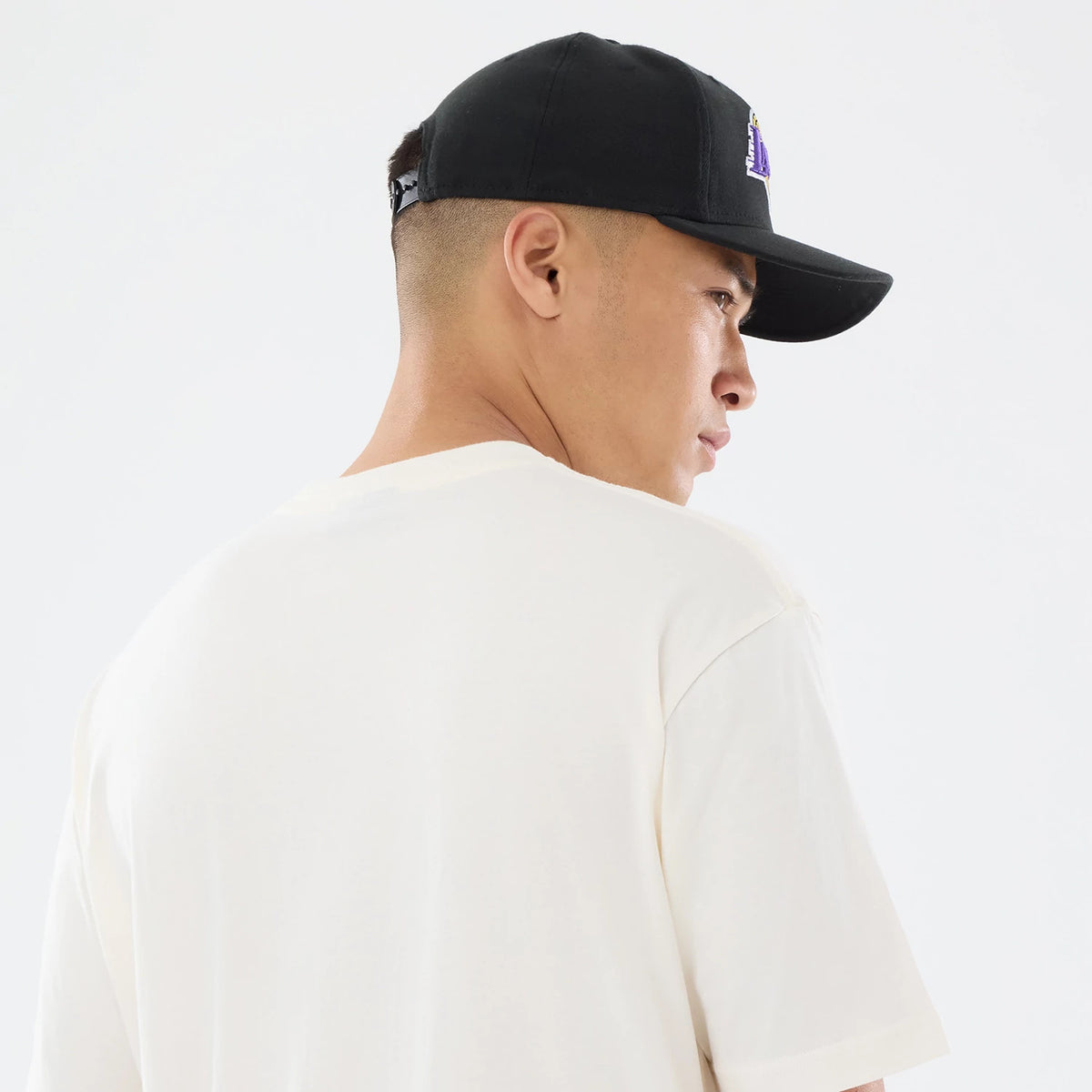 New Era LA Lakers NBA Sport Classic Cream T-Shirt, back view on a model styled with a black cap, showing a simple cream finish without graphics or text on the back, highlighting the t-shirt's relaxed fit and short sleeves.