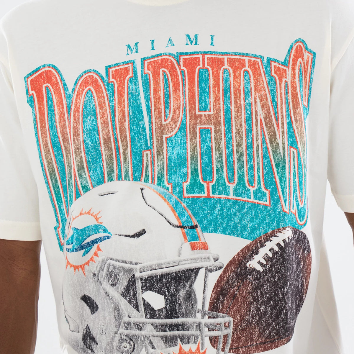 New Era Miami Dolphins NFL Sport Classic Cream T-Shirt, front view showing a large graphic with oversized distressed DOLPHINS lettering in orange and teal, a detailed print of a football helmet and ball, and the word MIAMI above the main graphic.