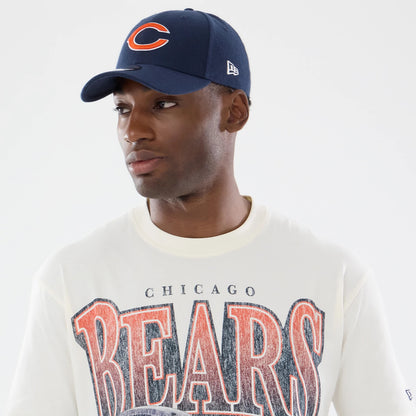 New Era Chicago Bears NFL Sport Classic Cream T-Shirt, front view on a model styled with a navy cap featuring an embroidered orange and white C logo on the front, while the shirt displays large Bears lettering in textured orange and navy print.
