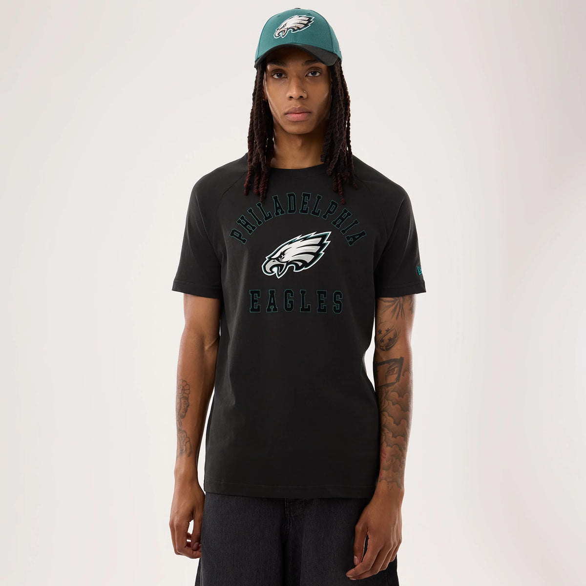 New Era Philadelphia Eagles NFL Sideline 2026 Black T-Shirt, front view on a model featuring large arched Philadelphia lettering above an embroidered Eagle's logo and Eagles wording below, with a teal New Era logo on the sleeve and a matching cap.