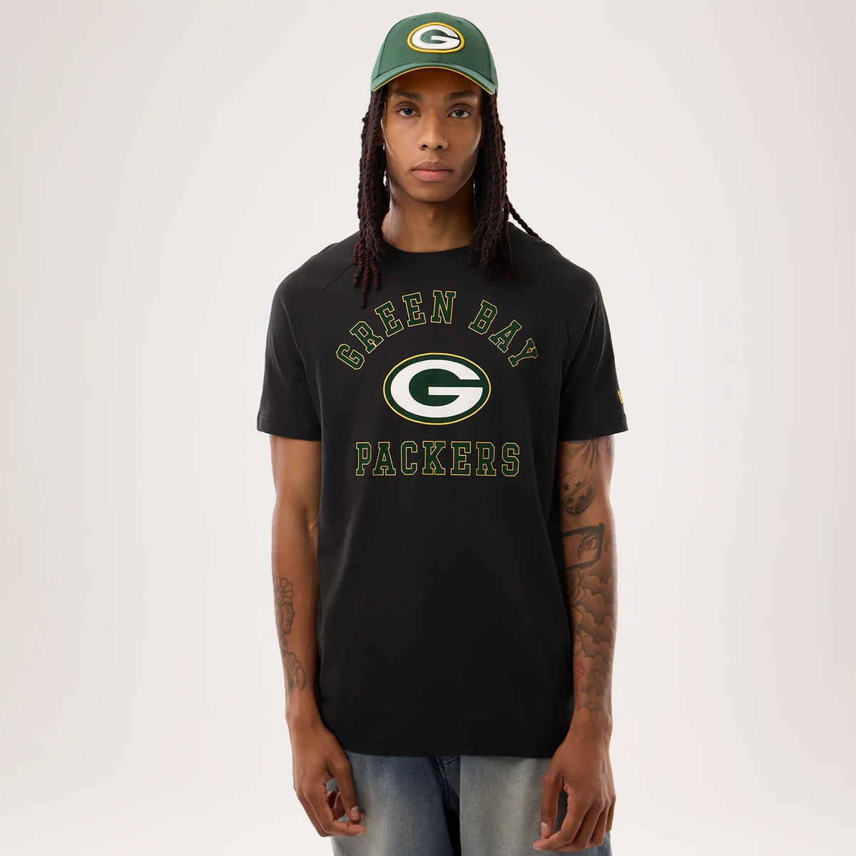 New Era Green Bay Packers NFL Sideline 2026 Black T-Shirt, front view on a model showing the Green Bay lettering and large central team logo in green and white on the chest, paired with a matching green cap featuring the Packers logo.