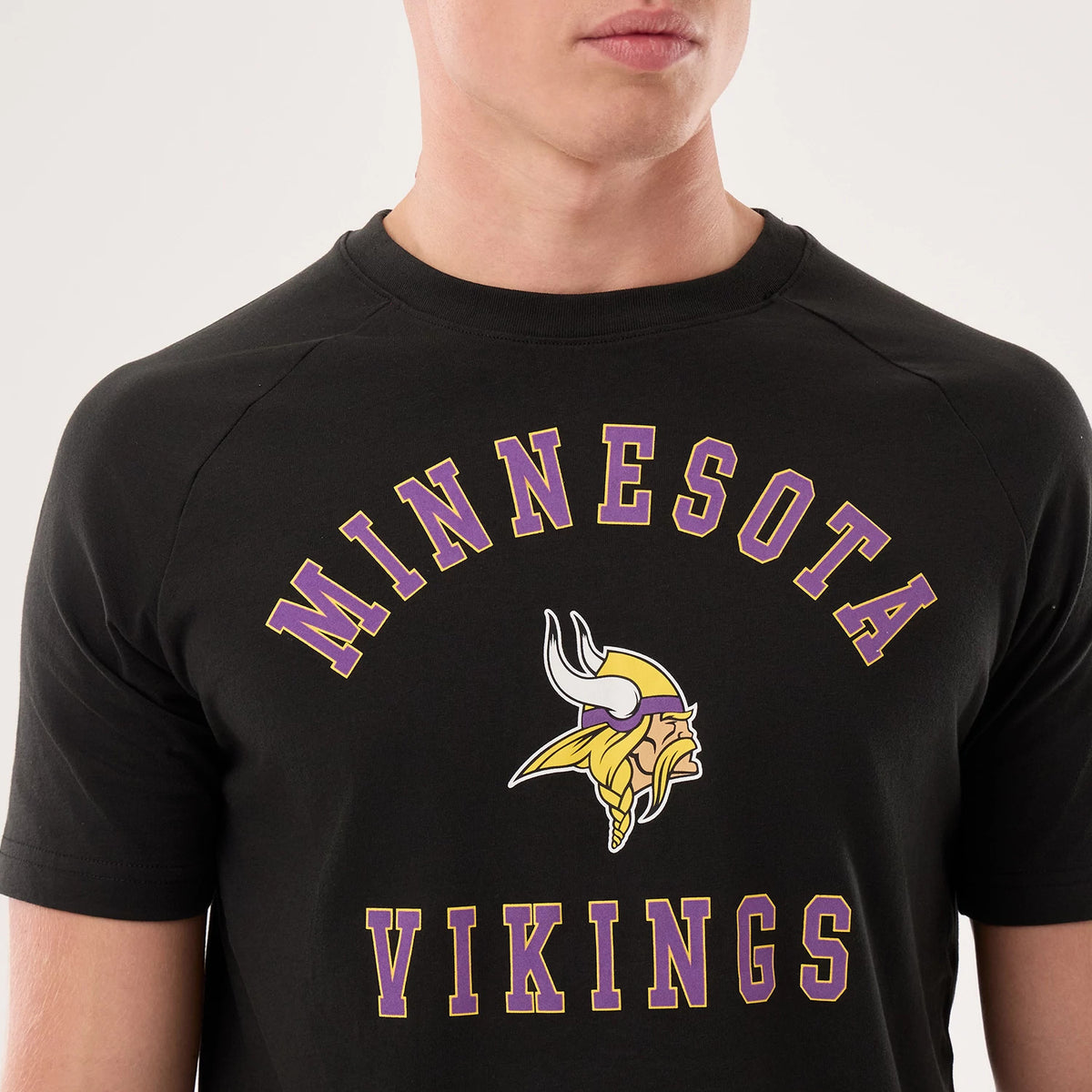 New Era Minnesota Vikings NFL Sideline 2026 Black T-Shirt, front view on-model showing the print with yellow and purple Minnesota Vikings lettering arched above and below a large printed Vikings logo on the chest, emphasising team pride.