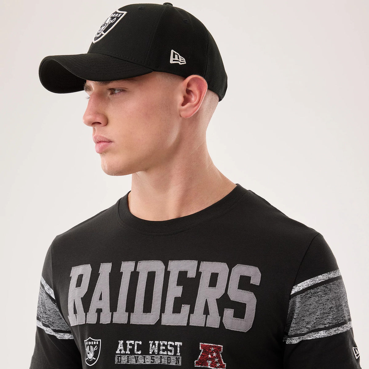 New Era Las Vegas Raiders NFL Sideline 2026 Black T-Shirt, on-model view displaying large grey embroidered RAIDERS lettering across the chest, detailed team and division logos beneath, and heathered stripe patterns on the sleeves.