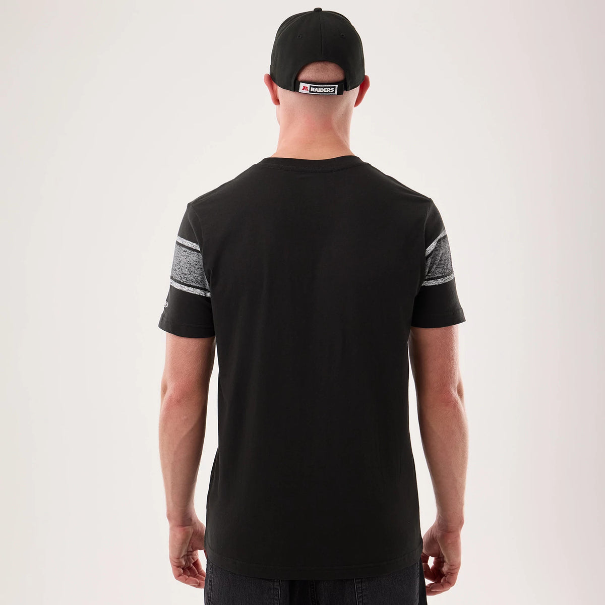 New Era Las Vegas Raiders NFL Sideline 2026 Black T-Shirt, back view on a model with a matching cap, featuring grey stripe on the sleeves, a simple black design across the back, and an embroidered NFL Raiders logo on the left sleeve.