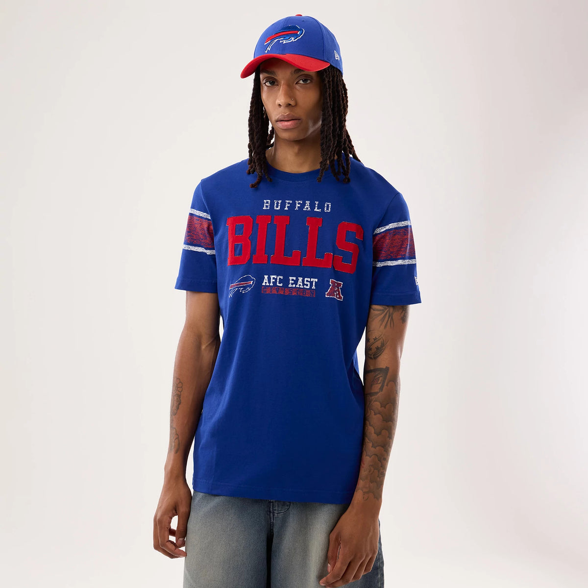 New Era Buffalo Bills NFL Sideline 2026 Blue T-Shirt, front view on-model featuring prominent red BILLS lettering across the chest, Buffalo Bills logo below it, and striped sleeve details in red and blue, paired with a matching cap.