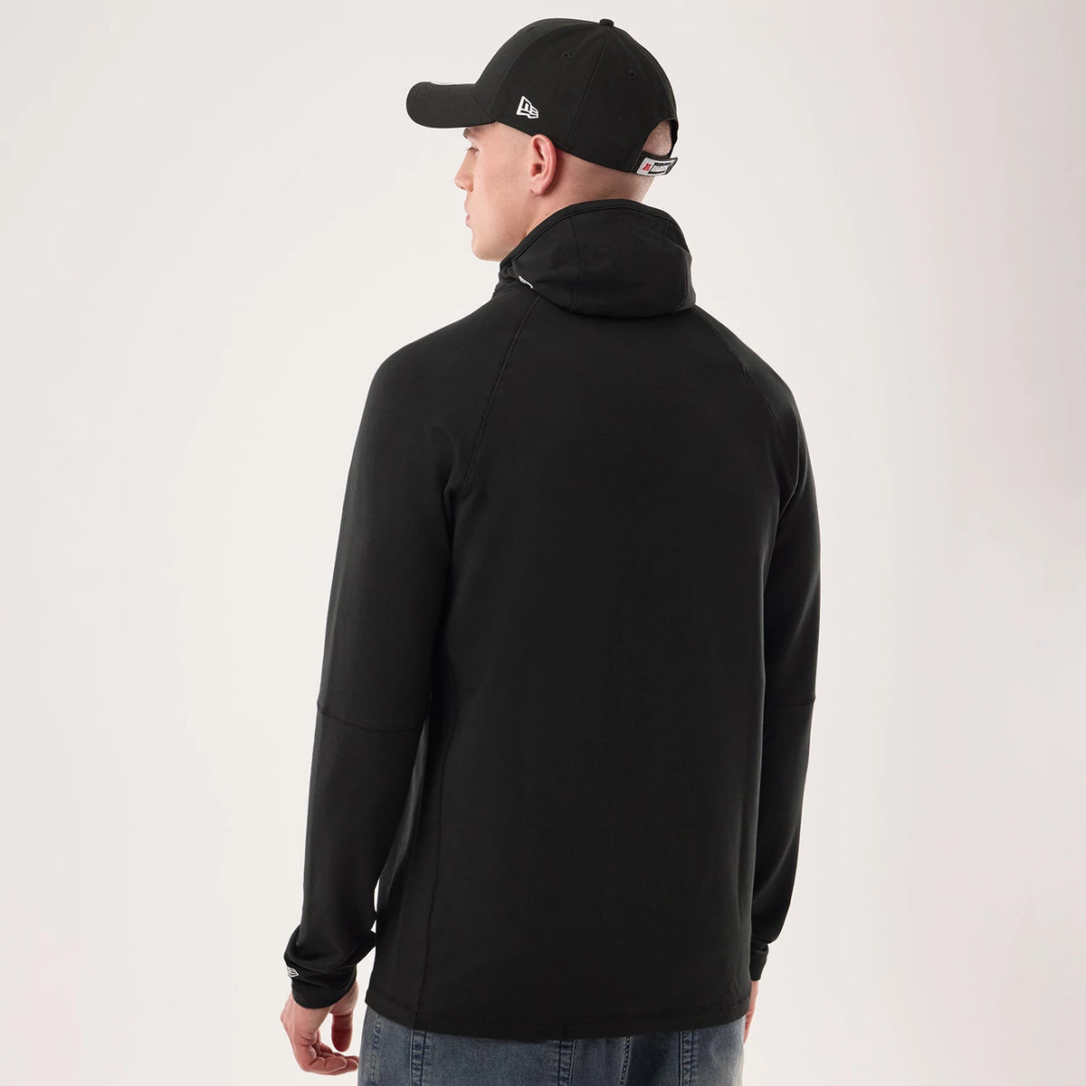 New Era Las Vegas Raiders NFL Sideline 2026 Black Balaclava Hoodie, back view on-model highlighting the black design with a raised hood, fitted long sleeves, and stitching, worn with a black cap featuring a raised New Era logo on the side.