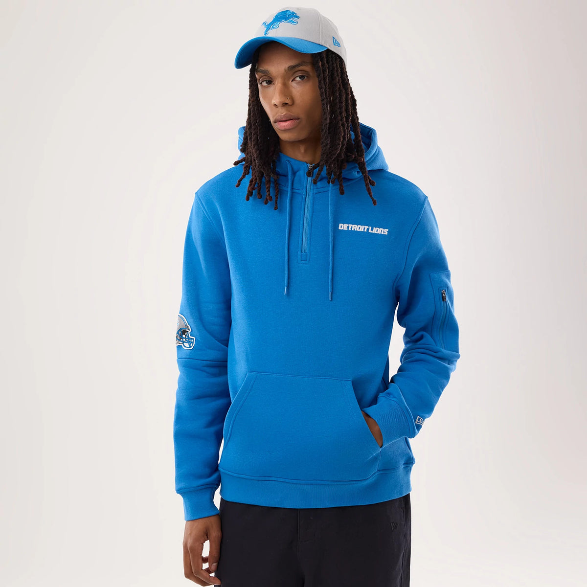 New Era Detroit Lions NFL Sideline 2026 Blue Pullover Hoodie, front view on a model, showcasing the blue colour, the white embroidered Detroit Lions logo on the chest, and a printed team emblem on the left sleeve above the cuff.