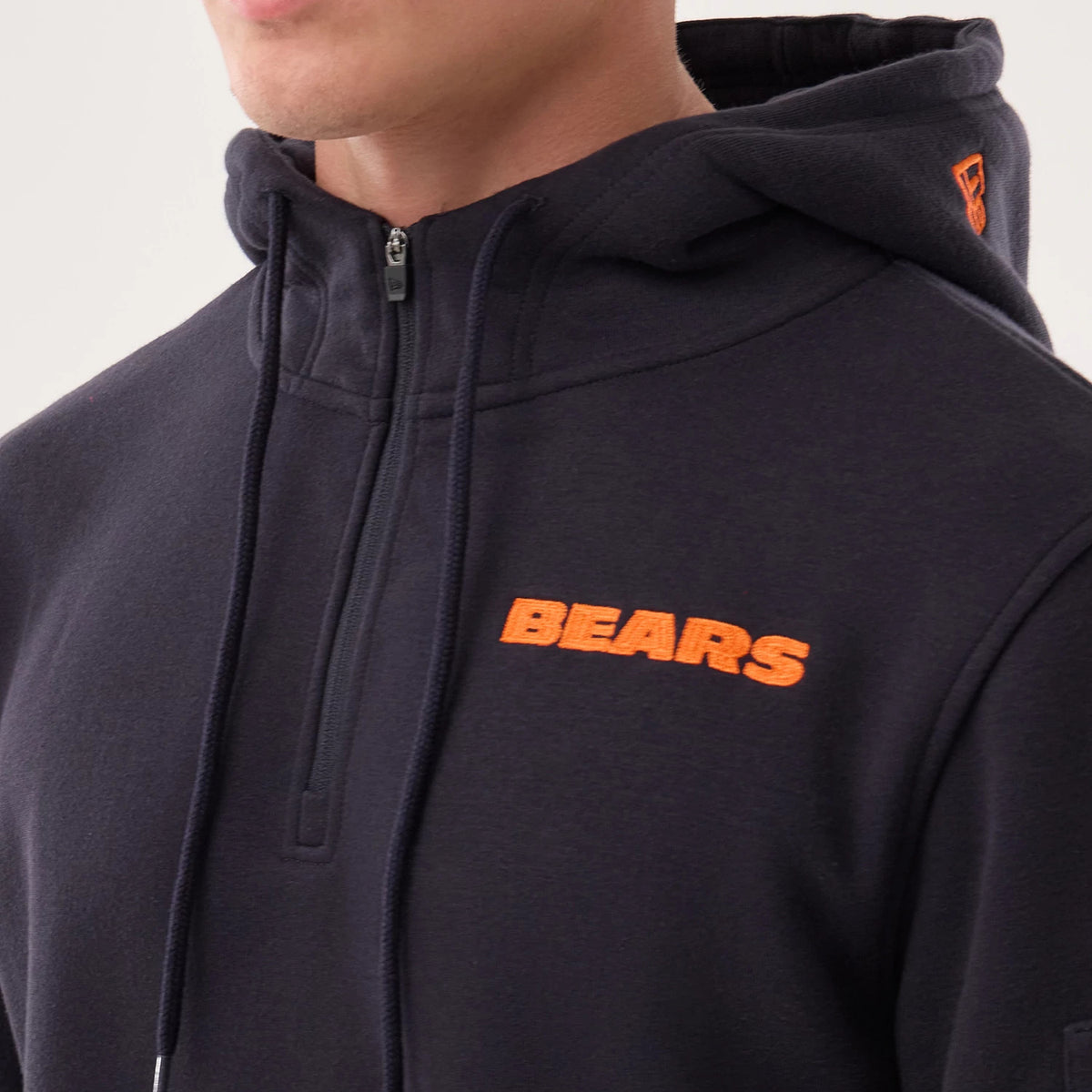 New Era Chicago Bears NFL Sideline 2026 Navy Pullover Hoodie, three-quarter view showing an orange embroidered BEARS logo on the left chest, a small orange embroidered New Era logo on the side of the hood, and a half-zip closure at the front.