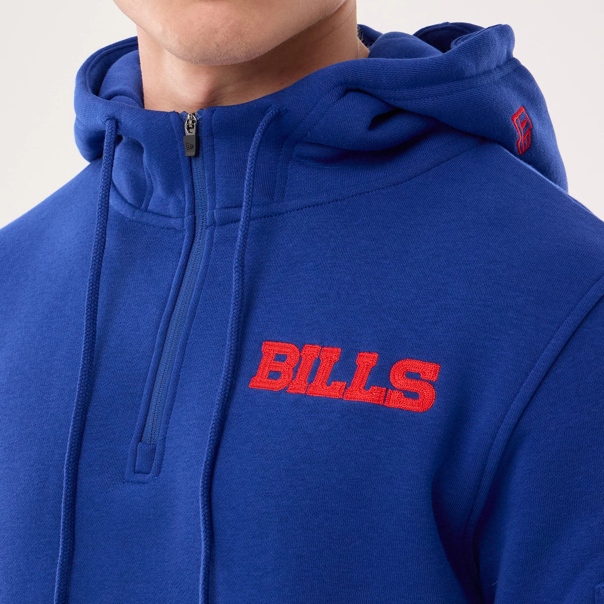New Era Buffalo Bills NFL Sideline 2026 Blue Pullover Hoodie, front view showing a large red embroidered BILLS logo on the chest, detailed stitching around the front zip and drawstrings, and a small red embroidered logo on the hood.
