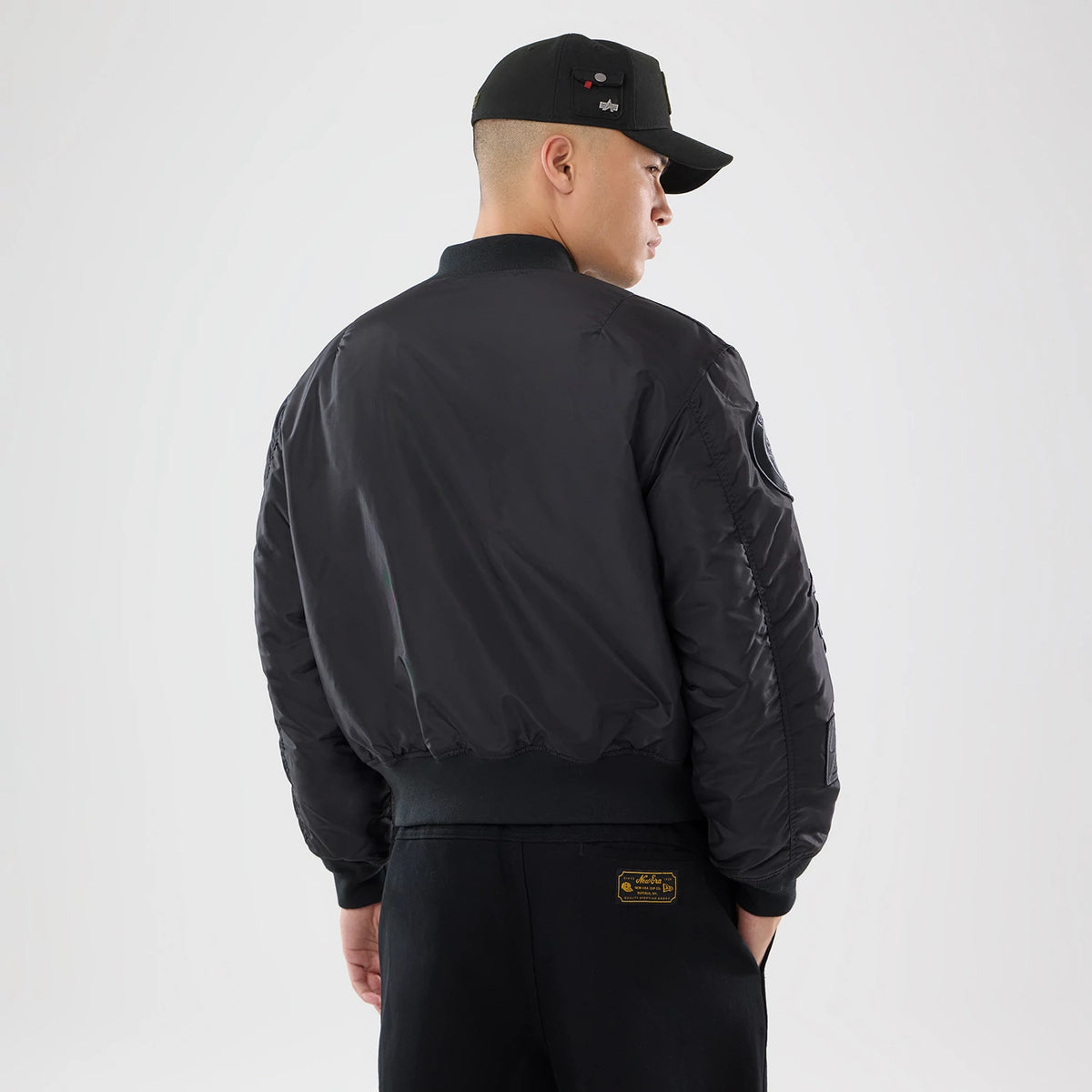 New Era New York Yankees MLB X Alpha Black Bomber Jacket & Tactical Vest, back view on a model showing the black back panel of the bomber jacket with a fitted waistband, a New Era logo on the cap, and near the shoulder.