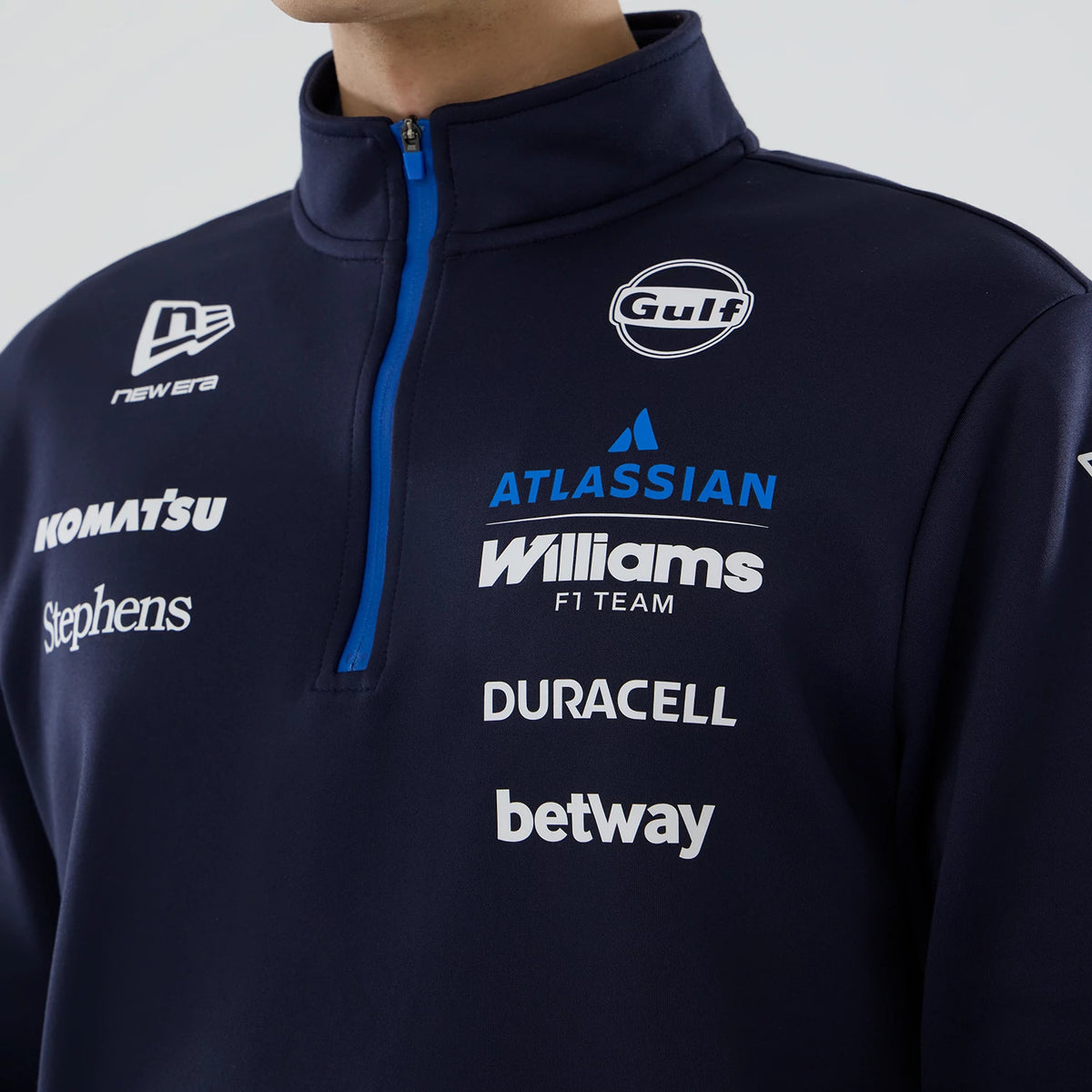 New Era Williams Navy Mid Layer 1/4 Zip Sweater, front view showing multiple sponsor logos including Gulf and Atlassian on the navy fabric, with a quarter-length zip featuring contrasting blue edging, worn by a model.