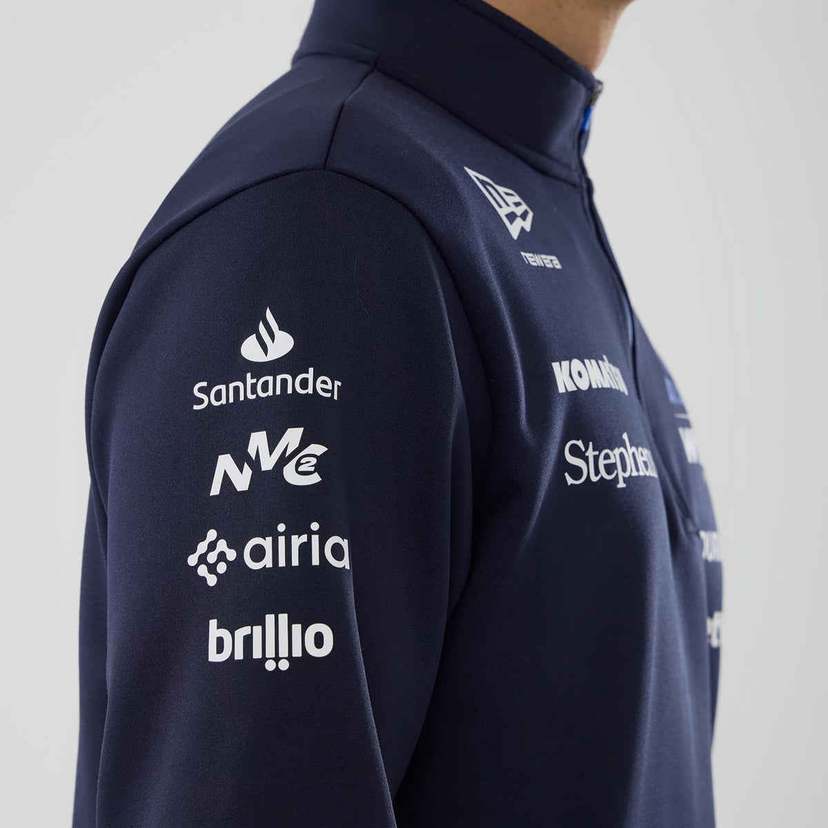 New Era Williams Navy Mid Layer 1/4 Zip Sweater, side view on a model showing multiple white sponsor logos down the left sleeve, the New Era flag logo on the right chest and a high collar in a navy fabric.