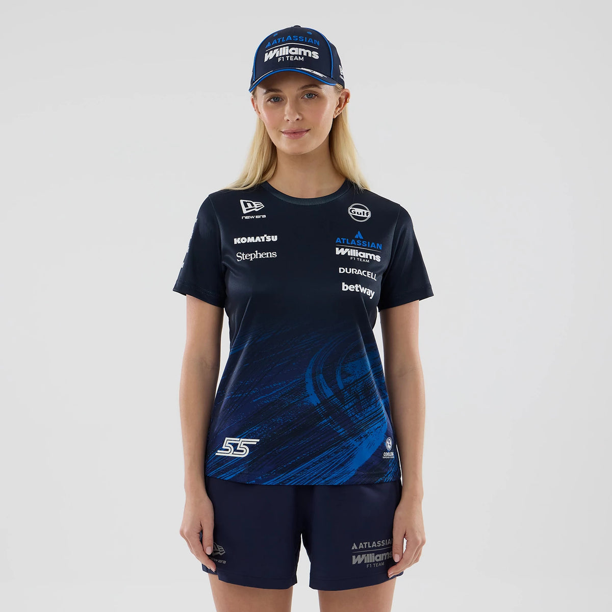 New Era Williams Womens Carlos Sainz Navy Tech T-shirt, front view on-model showing sponsor logos across the chest with a dynamic blue graphic design on the lower right, a white embroidered '55' near the hem and a matching cap worn by the model.