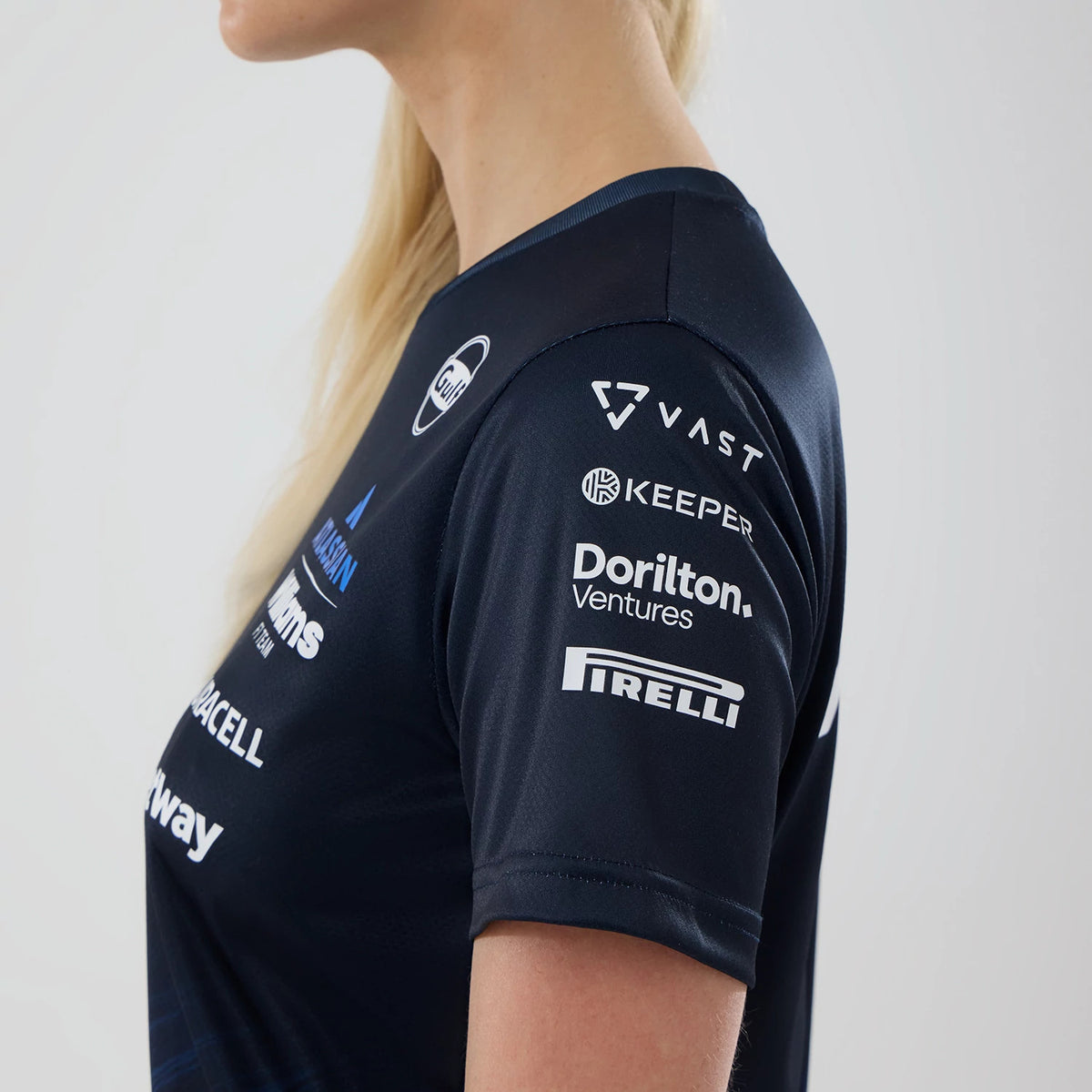 New Era Williams Womens Navy Tech T-shirt, side view on a model displaying multiple white printed sponsor logos, including Pirelli on the sleeve, with a close-fitting navy neckline and a cuff edge on the short sleeve.