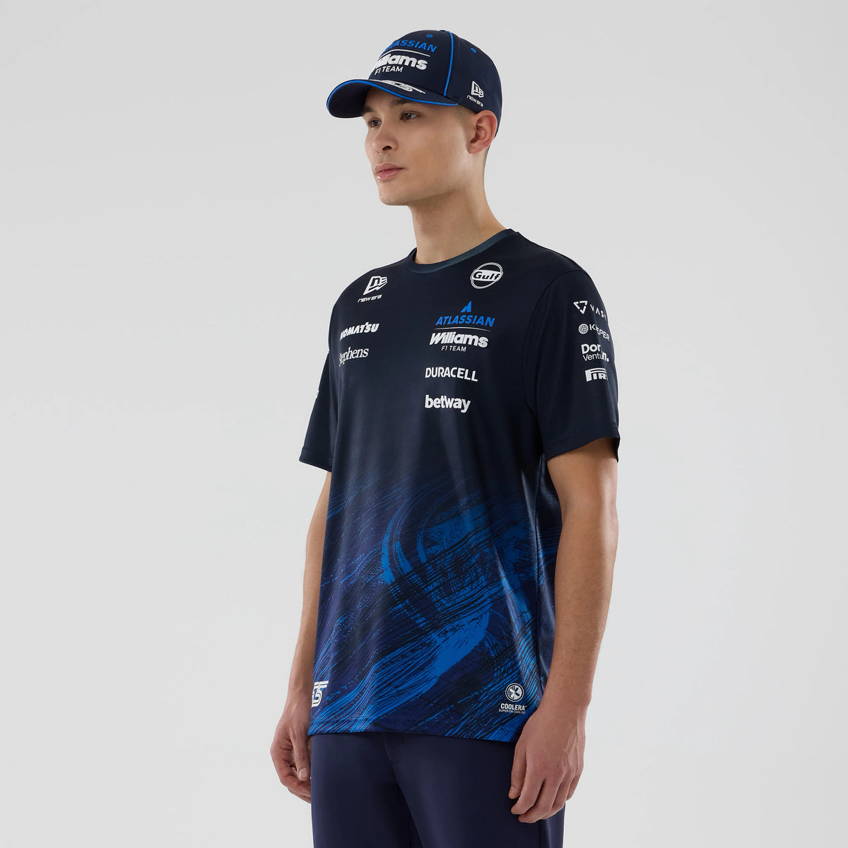 New Era Williams Carlos Sainz Navy Tech T-shirt, three-quarter view on a model wearing a navy cap, showcasing multiple sponsor logos across the chest and sleeves, with dynamic blue abstract graphics on the lower half of the navy tee.