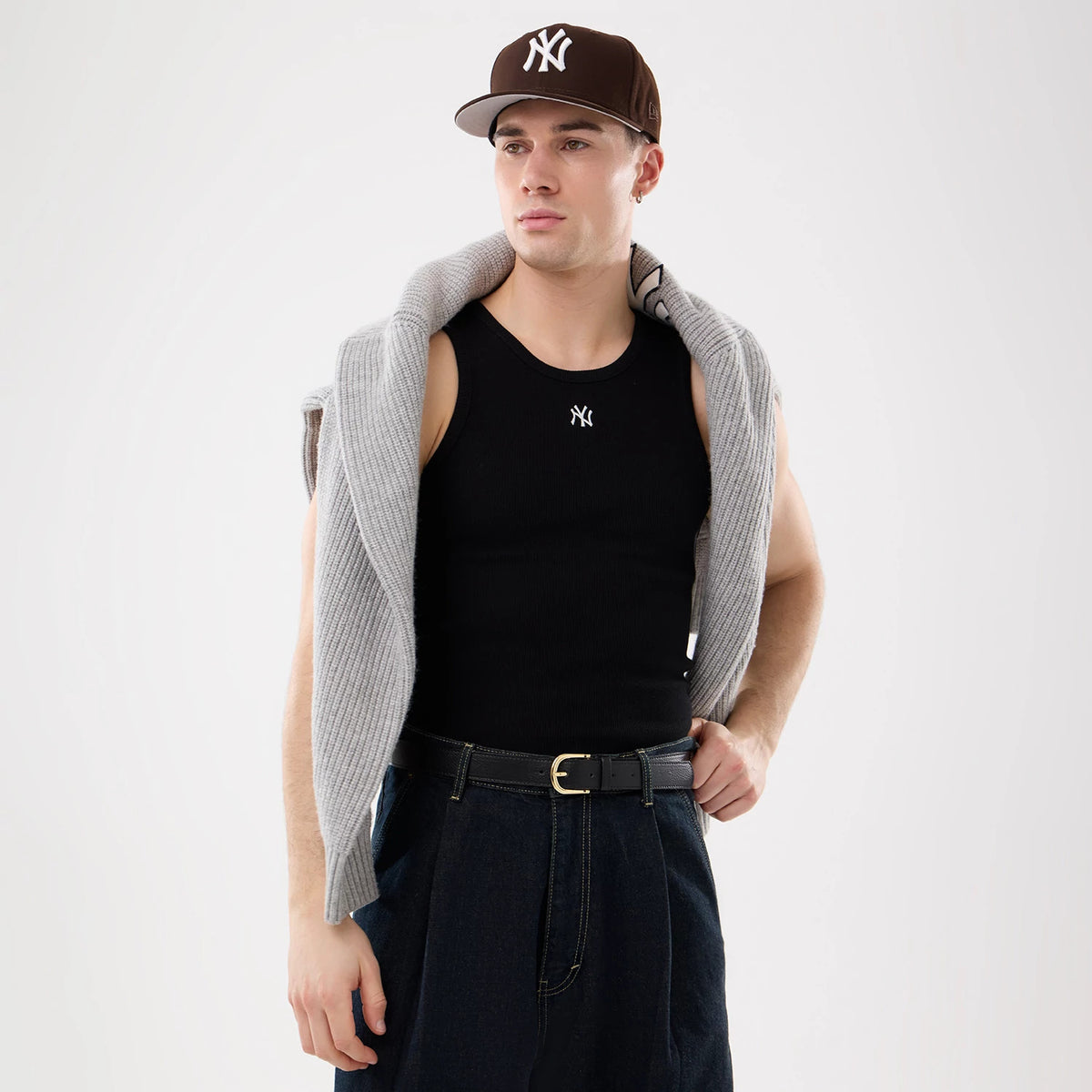 New Era New York Yankees MLB Rib Black Vest, on-model view styled with a grey knit sweater draped over the shoulders, featuring the NY logo on the chest, and paired with dark trousers and a brown fitted cap showcasing the front logo.