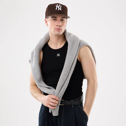New Era New York Yankees MLB Rib Black Vest, on-model view styled with a grey sweater draped over the shoulders, showing a small white Yankees logo on the black ribbed fabric, paired with dark jeans and a black belt.