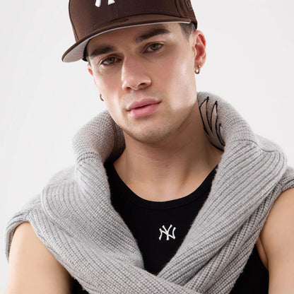 New Era New York Yankees MLB Rib Black Vest, on-model view showing a close-up of the black vest with an embroidered white NY logo on the chest, worn under a grey knitted scarf draped around the shoulders.