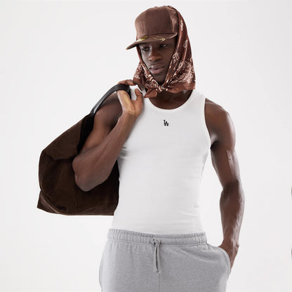 New Era LA Dodgers MLB Rib White Vest, front view on a model wearing a brown cap with a bandana, showing the black embroidered LA logo on the chest centre of the vest, paired with grey joggers and carrying a brown bag.