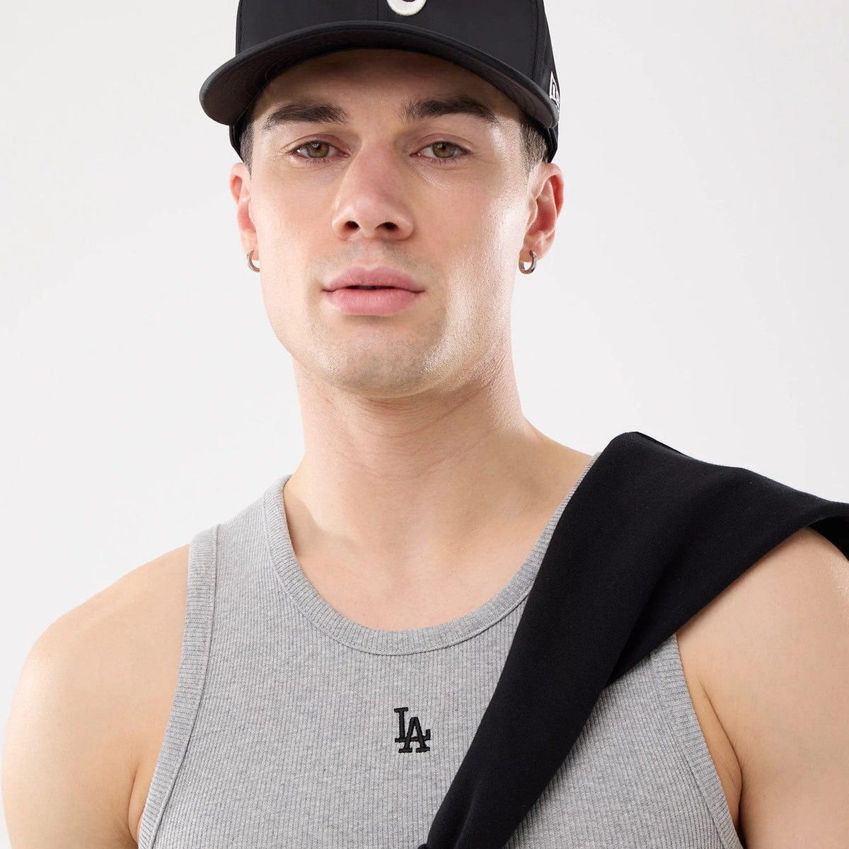 New Era LA Dodgers MLB Rib Grey Vest, front view on a model with a black cap, showing the black embroidered LA Dodgers logo centred on the ribbed grey fabric, complemented by a black garment draped over one shoulder.