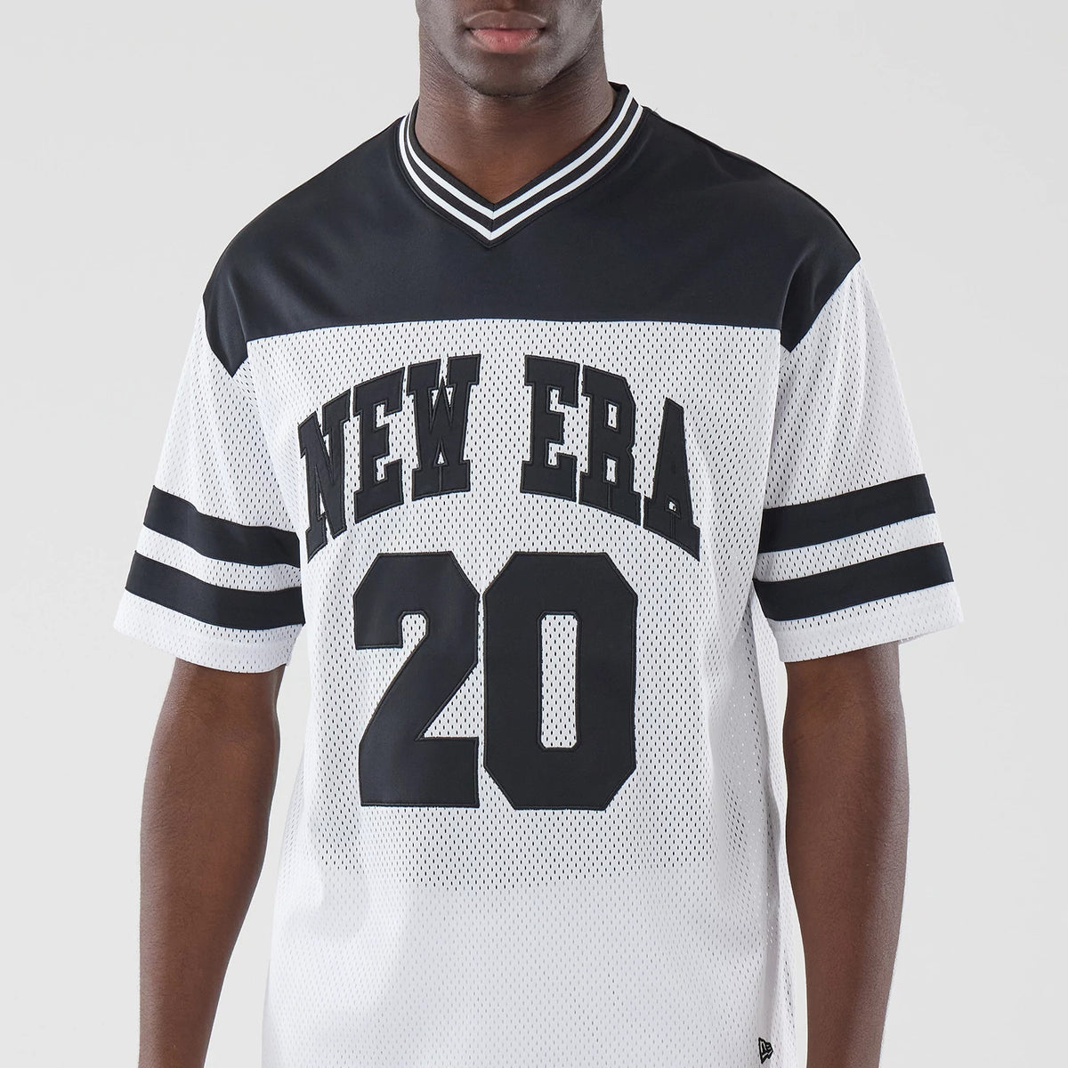 New Era Mesh White Oversized T-Shirt, front view on a model featuring large black New Era lettering across the chest, a black number 20 below, black shoulder panels, white mesh fabric, and double black stripes on both sleeves.