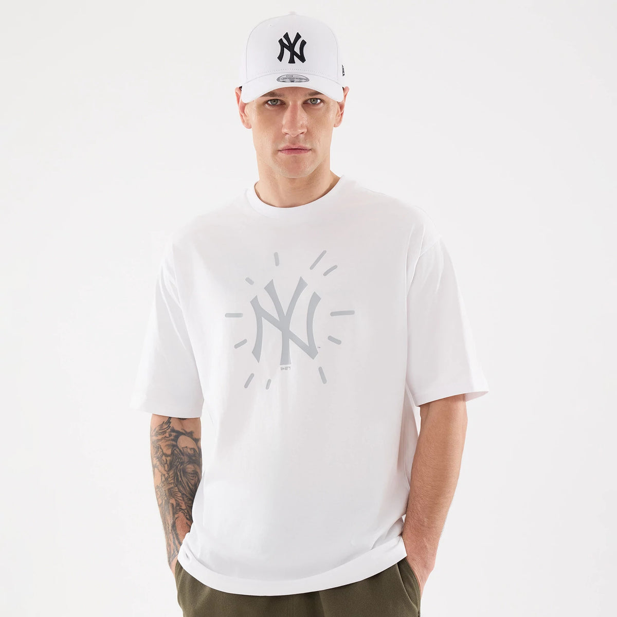New Era New York Yankees MLB 59FIFTY Day Graphic White T-Shirt, front view on a model also wearing a matching cap, displaying a large grey New York Yankees logo with sunburst graphic centred across the chest of the white short-sleeved tee.