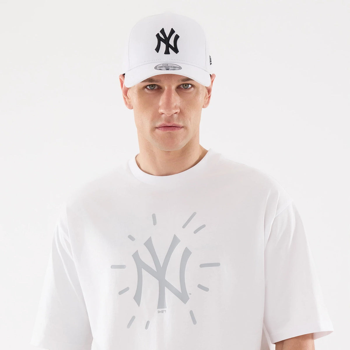 New Era New York Yankees MLB 59FIFTY Day Graphic White T-Shirt, front view on-model showing the large grey New York Yankees logo in the centre, short sleeves, and a white New Era cap with a black raised Yankees logo worn above.