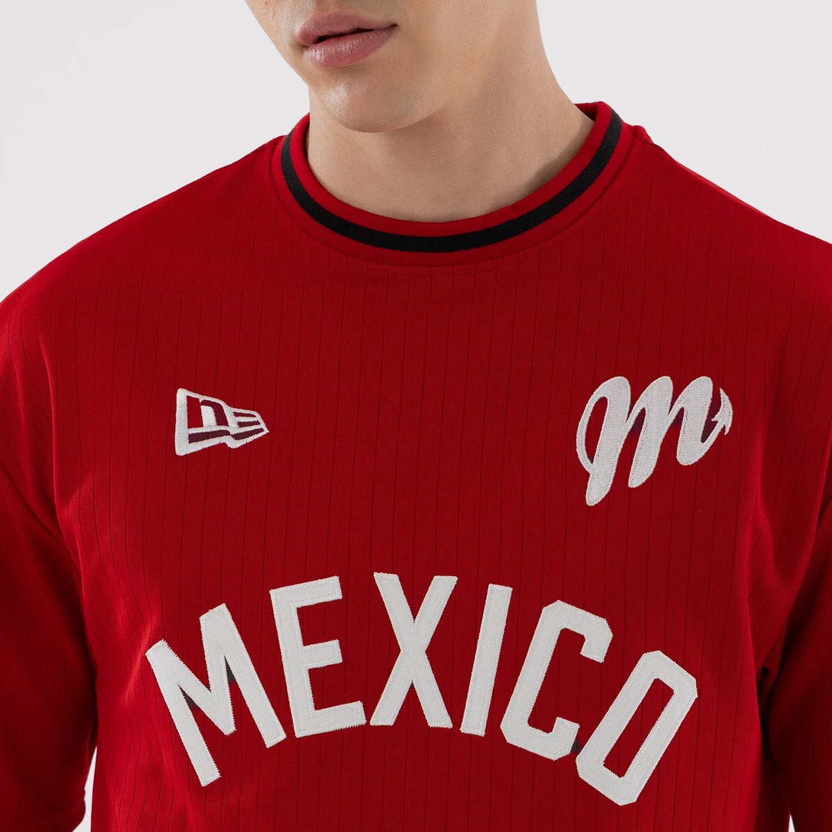 New Era Mexico Diablos LMB Red Oversized T-Shirt, front view on-model showcasing the red fabric with an embroidered white m logo on the chest, a New Era logo on the upper front, and MEXICO lettering across the chest under a striped neckline.