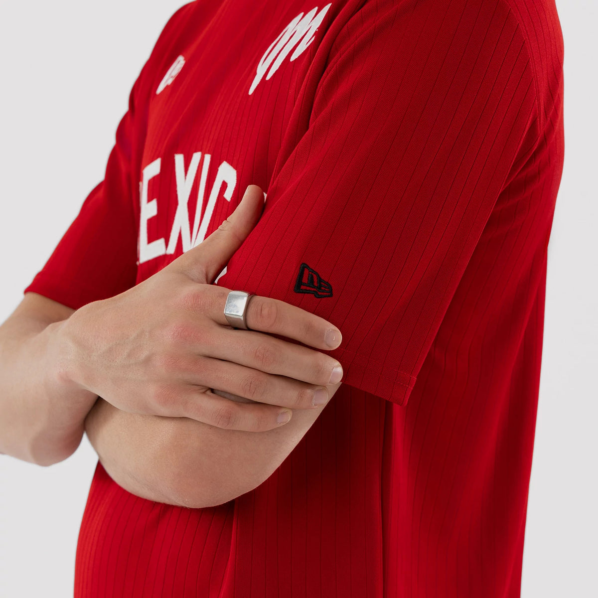 New Era Mexico Diablos LMB Red Oversized T-Shirt, side view showing the white 'MEXICO' lettering across the chest, with an embroidered New Era logo in black on the sleeve and worn by a model with crossed arms.