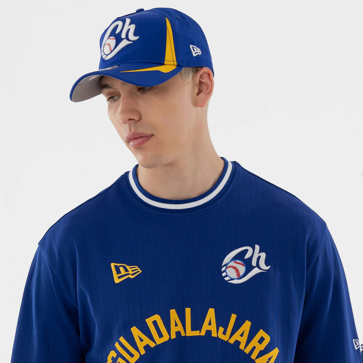 New Era Charros De Jalisco LMB Blue Oversized T-Shirt, front view on a model with a matching cap, displaying a white embroidered team logo on the chest, the New Era flag on the left side, and yellow Guadalajara lettering across the front.