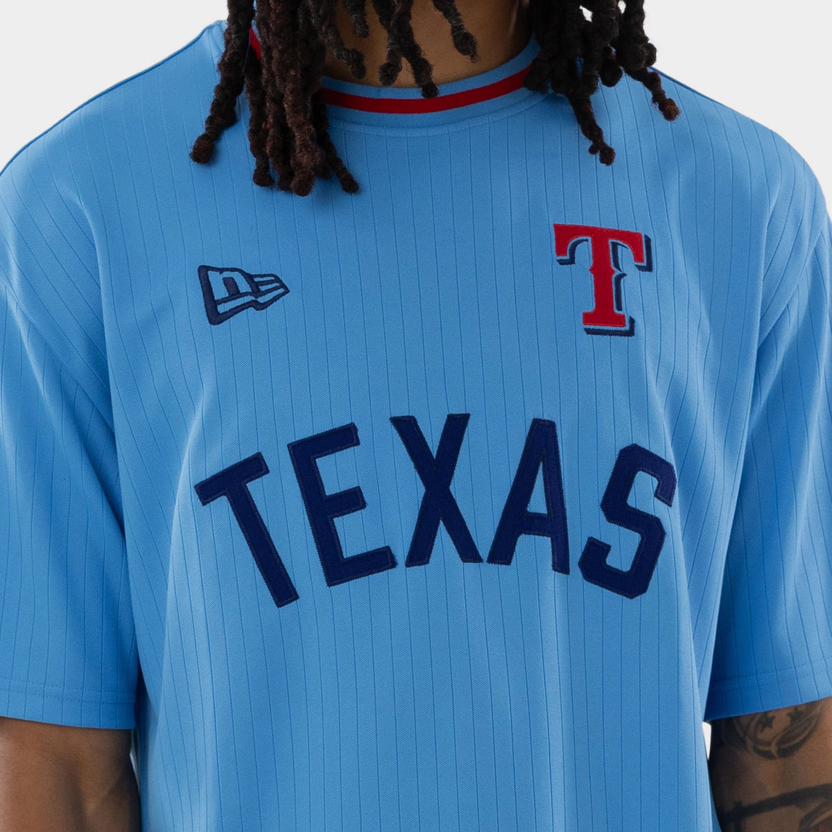 New Era Texas Rangers MLB Pastel Blue Oversized T-Shirt, front view on a model showcasing a blue pinstripe design, navy TEXAS lettering across the chest, an embroidered New Era logo on the shoulder, and a red T logo near the collar.