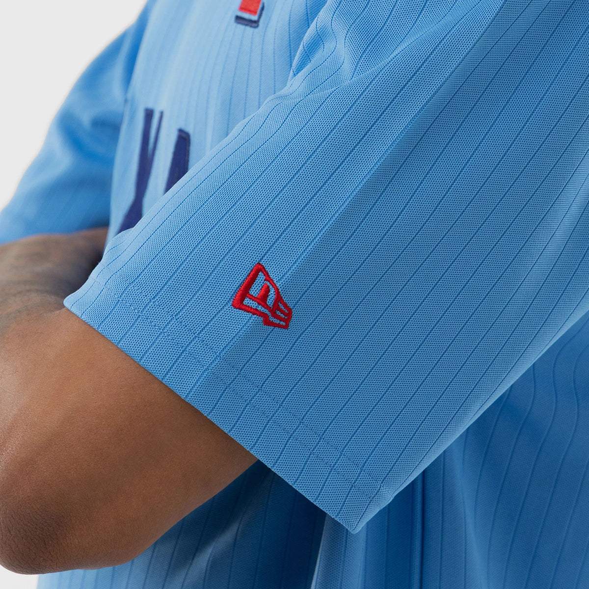 New Era Texas Rangers MLB Pastel Blue Oversized T-Shirt, side view showing the light blue fabric with vertical stripes, a red embroidered New Era logo near the short sleeve hem, and partially dark blue and red lettering across the chest.