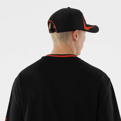 New Era San Francisco Giants MLB Black Oversized T-Shirt, back view on a model styled with a black cap, featuring an orange trimmed neckline, vertical pinstripes on the black fabric and a small embroidered logo on the sleeve edge.