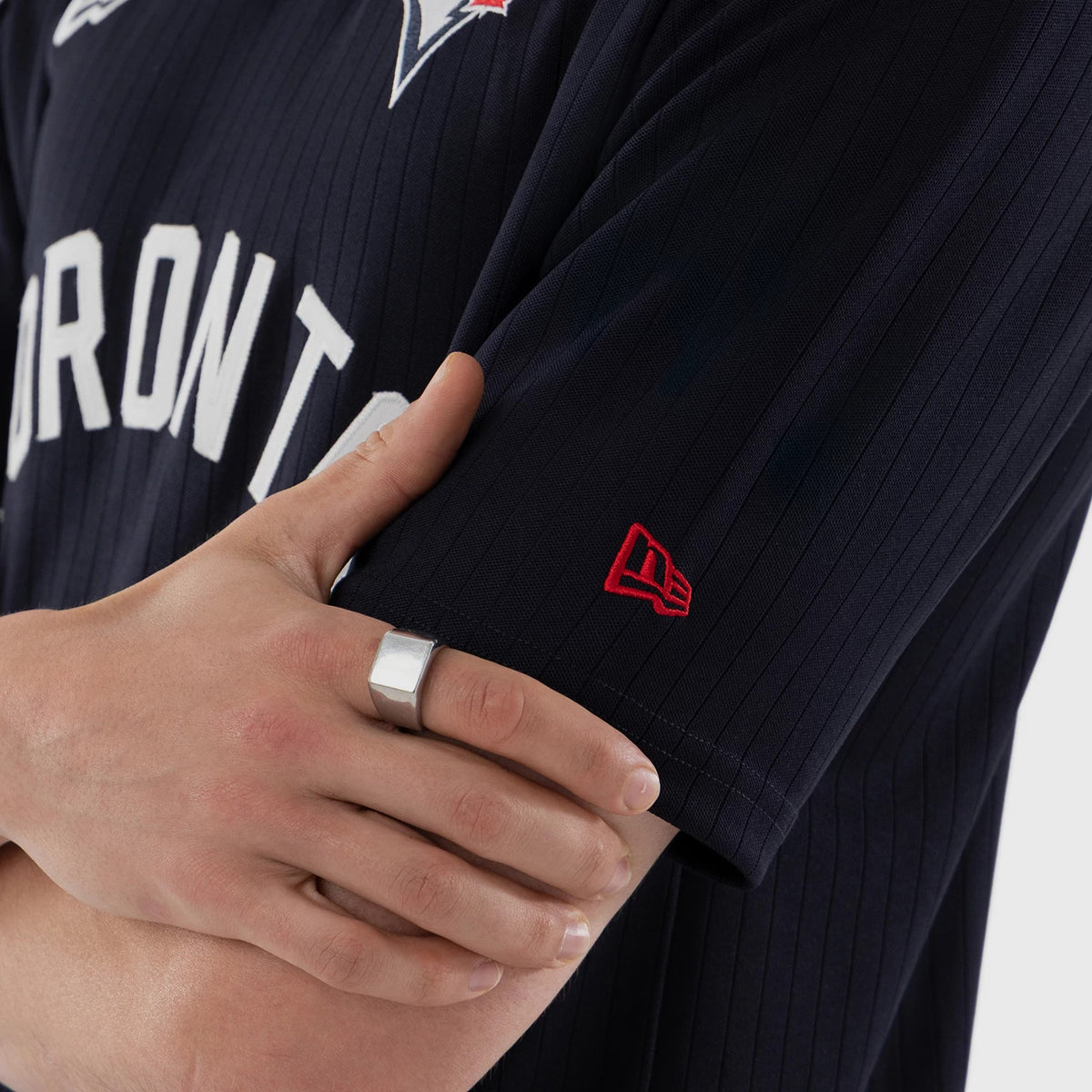 New Era Toronto Blue Jays MLB Navy Oversized T-Shirt, on-model view showing the right sleeve with a red embroidered New Era logo, navy fabric with pinstripes, and a view of white Toronto lettering across the chest.