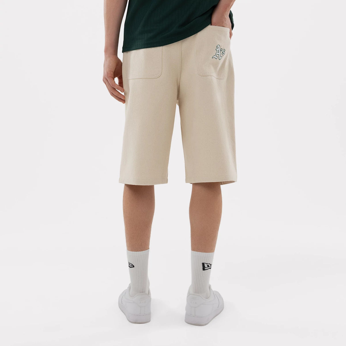 New Era Athletics MLB Jort Cream Oversized Shorts, back view on a model showing the cream-coloured shorts with two patch pockets, an embroidered A’s logo on the right pocket, paired with white socks featuring the New Era logo.