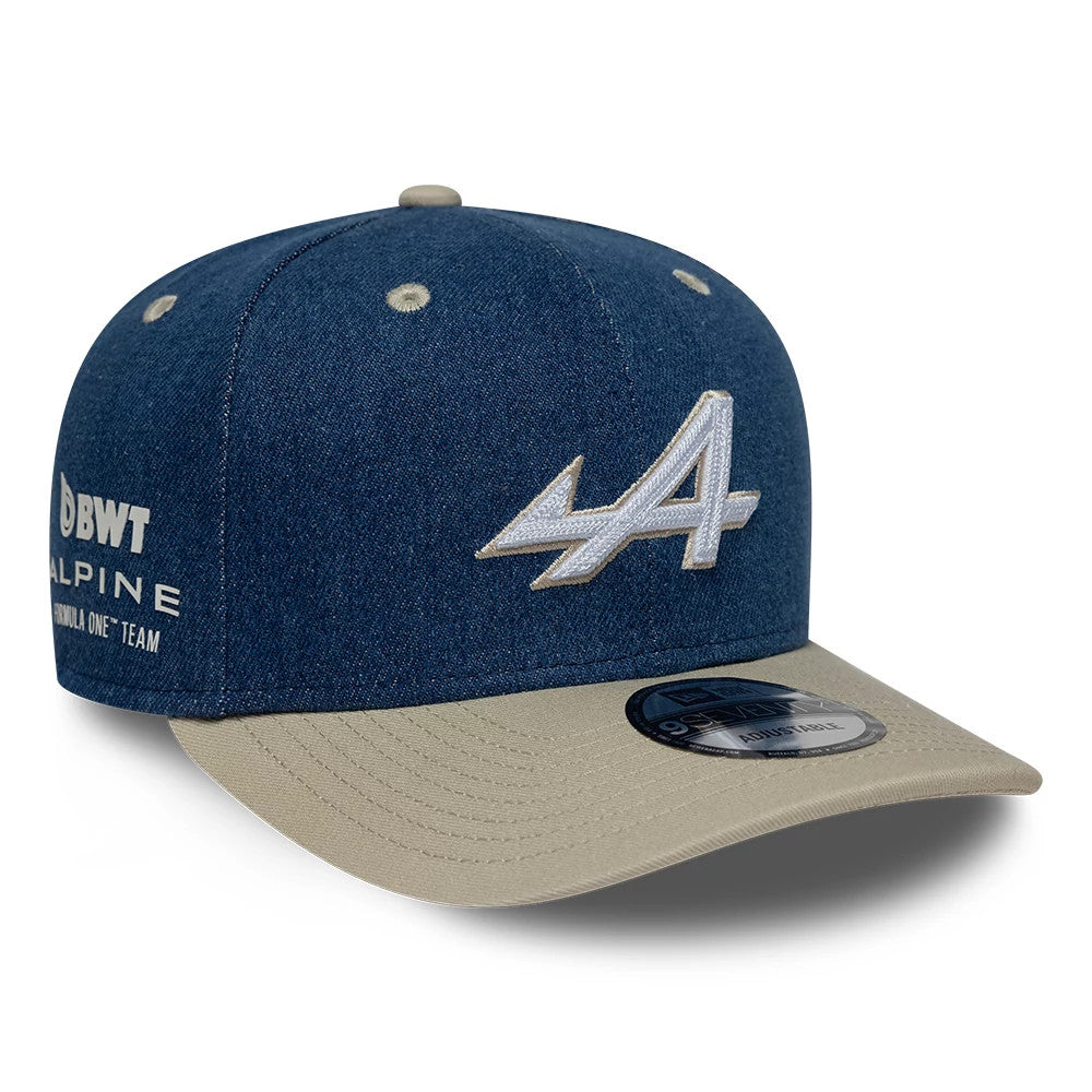 Alpine Racing Austin Race Special Denim Navy New Era 9SEVENTY Stretch Snap Adjustable Cap, three-quarter view showing the white embroidered A logo on the front panel, beige visor with a 9SEVENTY size sticker, and BWT Alpine logo on the left side.
