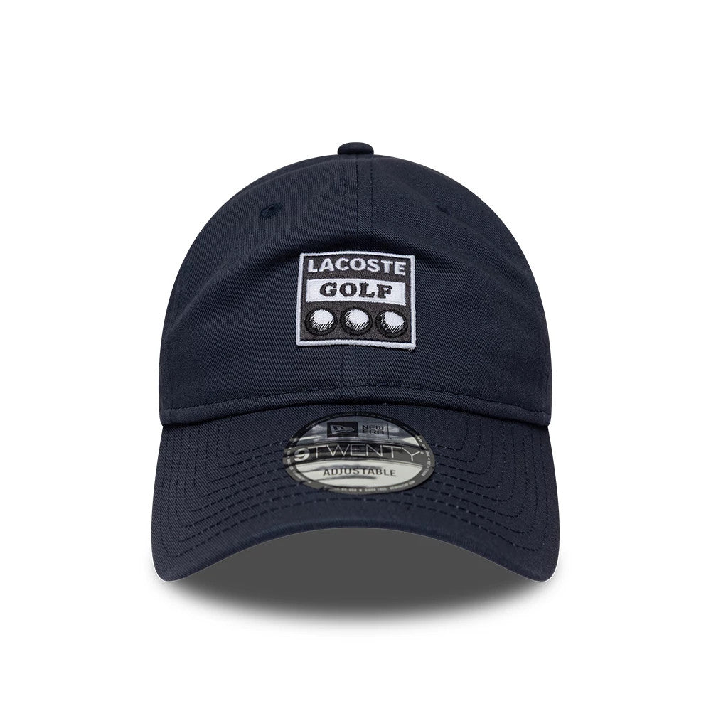 Lacoste X New Era Dark Blue 9TWENTY Adjustable Cap, front view showing a prominent white and dark blue Lacoste Golf patch on the front panel, a pre-curved visor with a 9TWENTY size sticker, and embroidered eyelets on the crown.