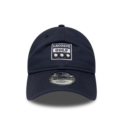 Lacoste X New Era Dark Blue 9TWENTY Adjustable Cap, front view showing a prominent white and dark blue Lacoste Golf patch on the front panel, a pre-curved visor with a 9TWENTY size sticker, and embroidered eyelets on the crown.