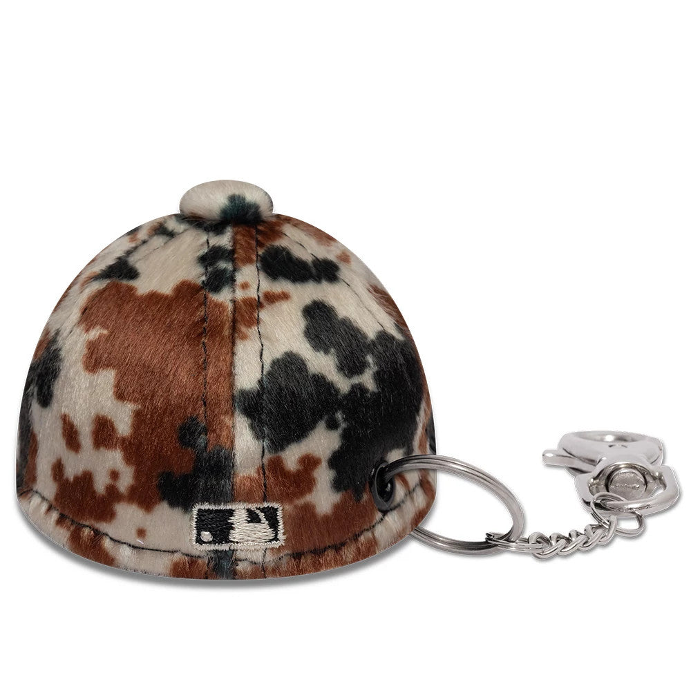 New Era New York Yankees MLB Animal Mini Cap Brown Key Chain, rear view showing the embroidered MLB Batterman logo at the centre back, featuring a cowhide pattern with brown, black, and white patches, and a silver keychain attachment.