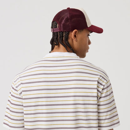New Era Stripe White T-Shirt, back view on-model showing the white shirt with horizontal stripes in shades of black, yellow, and burgundy, styled with a burgundy and beige cap worn backwards, highlighting the casual, streetwear look.
