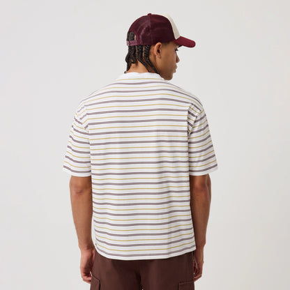 New Era Stripe White T-Shirt, back view showing horizontal stripes in purple, green, and mustard across the white fabric, worn by a model pairing it with a burgundy and white cap and brown trousers.