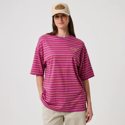 New Era Stripe Bright Purple T-Shirt, front view on-model showcasing horizontal yellow stripes across the bright purple fabric, complemented by an embroidered New Era logo on the left chest, styled with beige trousers and a beige cap.